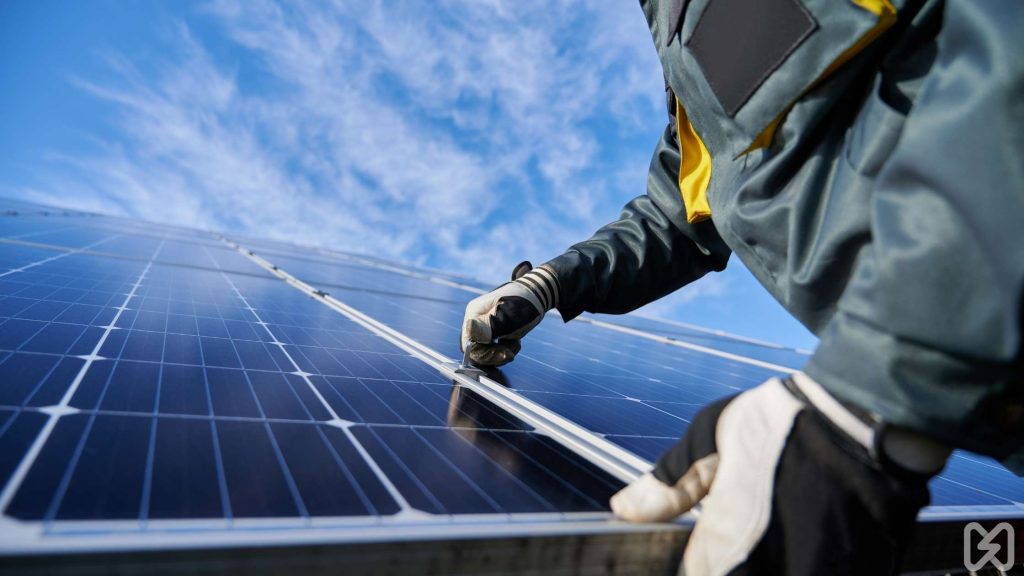 A technician securing solar panels under bright blue skies. Discover the role of installation in the cost of solar panels South Africa.